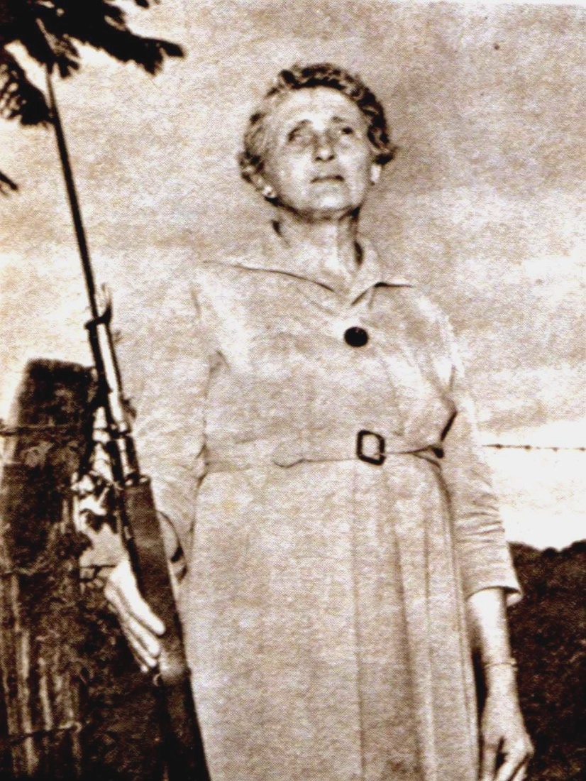 Maria Sguassábia de vestido, segurando uma espingarda